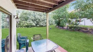 Eine überdachte Terrasse mit Glastisch und -stühlen, einer Holzzahlende und Blick auf einen gepflegten Rasen und Bäume.