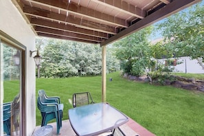 A covered patio with a glass table and chairs, a wooden ceiling, and a view of a well-maintained lawn and trees. - Dog-Friendly Condo with Patio, Full Kitchen, W/D, & Free WiFi (Bartlett)