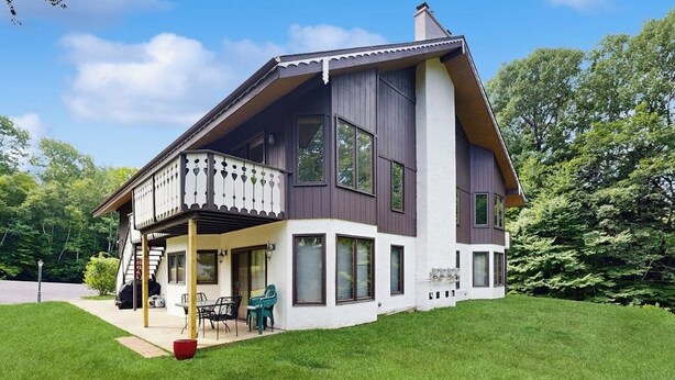 Ein zweistöckiges Haus mit Balkon, großen Fenstern und einem gepflegten Rasen.