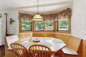 A dining area with a wooden table, chairs, and a bench. There are three windows with curtains, and a hanging light fixture. - Dog-Friendly Condo with Patio, Full Kitchen, W/D, & Free WiFi (Bartlett)