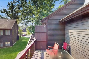 A deck with a table and chairs, a wooden fence, and a house with a sloped roof. - Cozy Condo with Shared Pool, High-Speed WiFi, W/D, Partial AC (Bartlett)