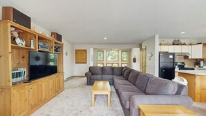 Olohuoneessa on kulmasohva, televisio, joka on sijoitettu puiseen kaappiin, sekä keittiöalue, jossa on jääkaappi.