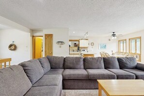 A living room with a sectional sofa, a wooden coffee table, and a kitchen area in the background. - Cozy Condo with Shared Pool, High-Speed WiFi, W/D, Partial AC (Bartlett)