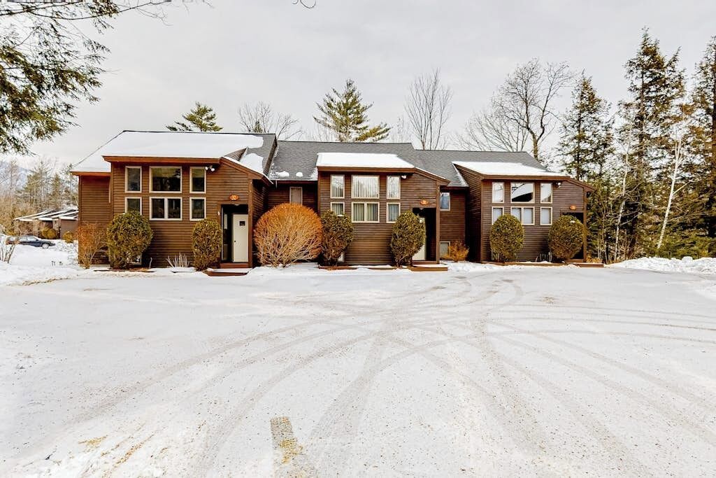 A two-story house with a garage, surrounded by snow-covered ground and trees.