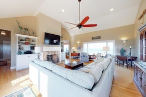 A spacious living room with a sofa, a television, a fireplace, and a ceiling fan. - Oceanfront Stunner w/ Kayaks, Beach Gear, Fireplace, Amazing Water Views & Pond (Rye)