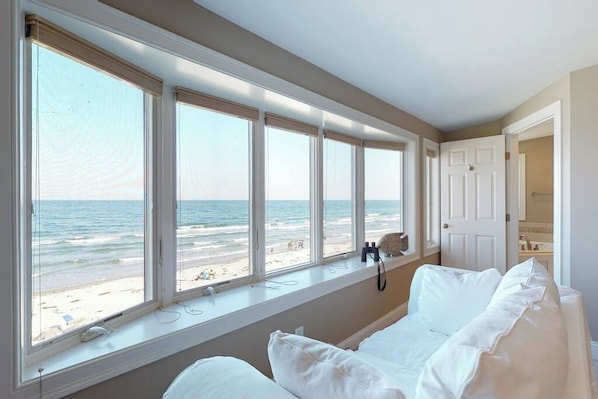 A bedroom with a large window overlooking the beach, a bed, and a door leading to a bathroom. - Oceanfront Stunner w/ Kayaks, Beach Gear, Fireplace, Amazing Water Views & Pond (Rye)