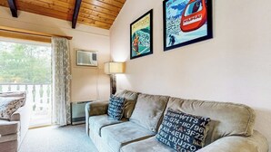 En stue med en sofa, to puder med alfanumeriske koder, en lampe, et vindue med gardiner og to indrammede plakater på væggen.