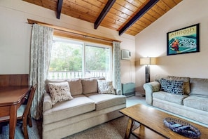 A cozy living room with a sofa, a coffee table, a TV, and a window with curtains. - Sweet condo with fast WiFi, gas fireplace, & W/D - close to slopes (Bartlett)