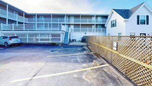 A multi-story building with balconies, a parking area, and a fenced section. - 2nd-floor studio 1 block from the beach with pool, beach access, grills, & W/D (Hampton)