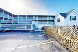 A multi-story building with balconies, a parking area, and a fenced section. - 2nd-floor studio 1 block from the beach with pool, beach access, grills, & W/D (Hampton)