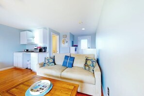 A living room with a sofa, coffee table, and a kitchen area with cabinets and appliances. - 2nd-floor studio 1 block from the beach with pool, beach access, grills, & W/D (Hampton)