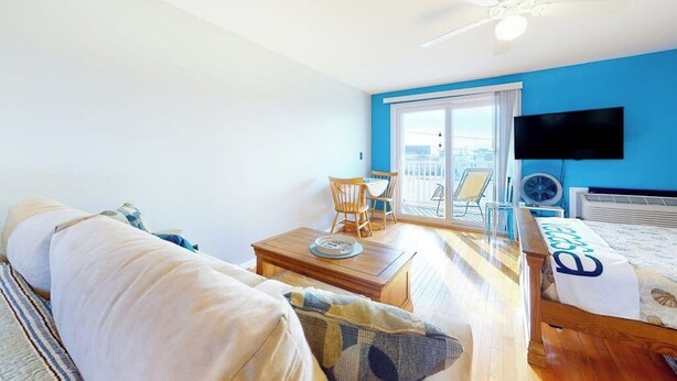 A room with a bed, a TV, a ceiling fan, a table, and a balcony with chairs. - 2nd-floor studio 1 block from the beach with pool, beach access, grills, & W/D (Hampton)