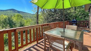 Una terraza con mesa de vidrio y sillas de mimbre, un paraguas verde y barandilla de madera con el letrero 'LOVE LAUGHTER'.