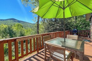 A deck with a glass table and wicker chairs, a green umbrella, and a wooden railing with 'LOVE LAUGHTER' sign. - Secluded mountain getaway with private sauna, large deck, sweeping views & WiFi (Bartlett)