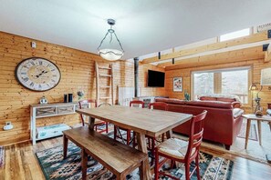 A wooden interior with a dining table, chairs, a red sofa, and a TV mounted on the wall. - Secluded mountain getaway with private sauna, large deck, sweeping views & WiFi (Bartlett)