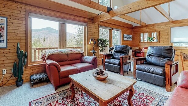 Interior acogedor de una cabaña con paredes de madera, ventanas amplias, un sofá de cuero rojo, una mesa de centro de madera y una planta de cactus.