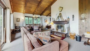 Un salón acogedor con techo de madera, chimenea y sofá con cojines estampados.