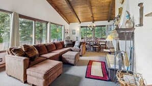 Una sala de estar acogedora con techo de madera, ventanas grandes, chimenea y comedor.