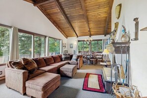 A cozy living room with a wooden ceiling, large windows, a fireplace, and a dining area. - Dog-friendly home with stunning views & balcony, near Cannon Mountain (Franconia)