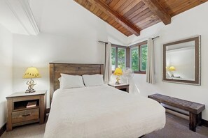 A bedroom with a large bed, wooden headboard, two bedside tables with lamps, a bench, a window with curtains, and a mirror on the wall. - Dog-friendly home with stunning views & balcony, near Cannon Mountain (Franconia)