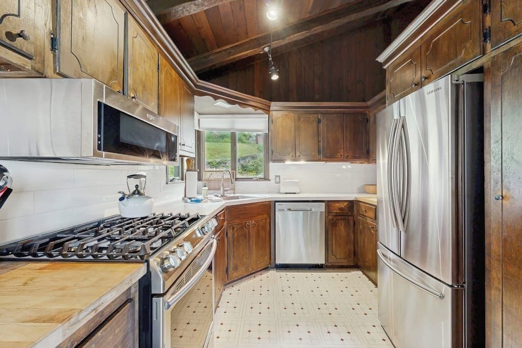 A kitchen with wooden cabinets, stainless steel appliances, and a view to the outdoors.