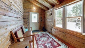 Ein rustikales Blockhaus-Interieur mit einer Holzbänkl, einem Teppich und einem Fenster mit Blick auf Schnee.