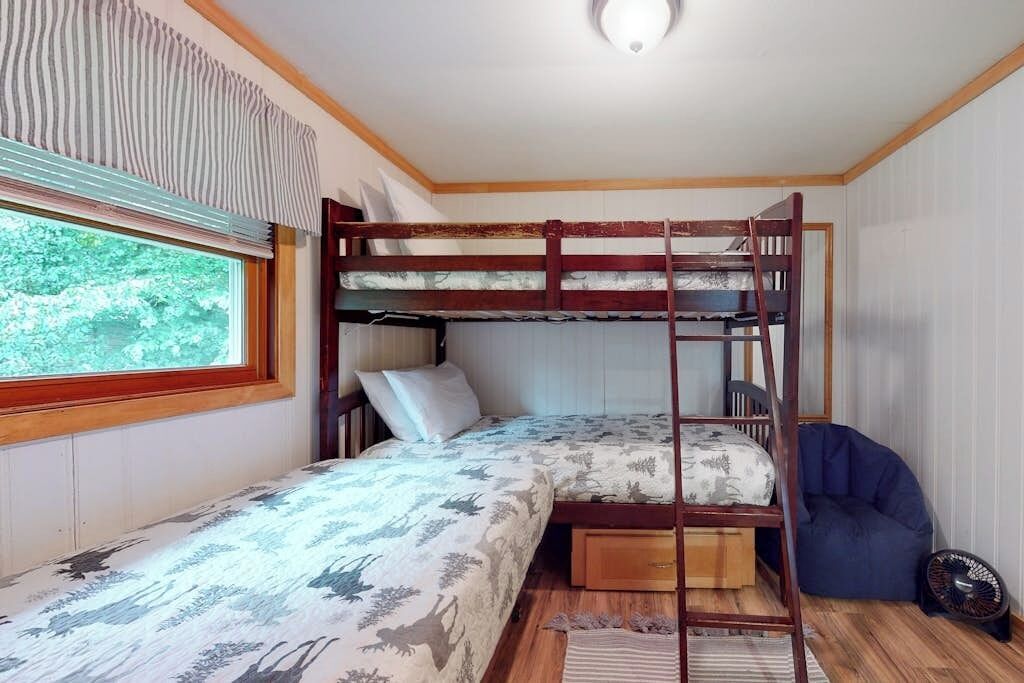 Een slaapkamer met stapelbed, raam, ventilator en een relax fauteuil.