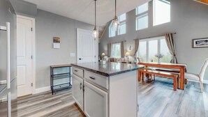 Una cucina moderna con isola centrale, illuminazione a sospensione e zona pranzo con tavolo e sedie in legno.
