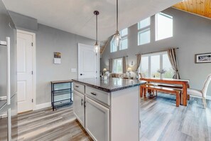 Eine moderne Küche mit einer zentralen Kochinsel, Pendelleuchten und einem Essbereich mit einem Holztisch und Stühlen.