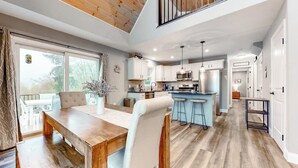 Cucina spaziosa con elettrodomestici moderni, zona pranzo con tavolo e sedie in legno e vista all'esterno tramite ampie finestre.
