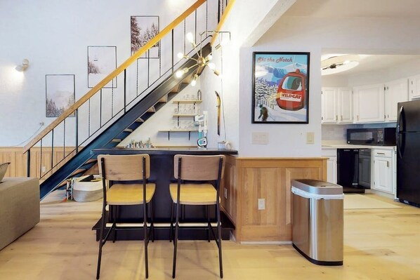 A modern kitchen with white cabinets, a black refrigerator, and a wooden staircase. - Christmas Mountain two-story condo with pool table, a mile from Story Land (Bartlett)