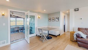 Ein modernes Wohnzimmer mit Glastür zum Patio, einem weißen Sofa, einem Esstisch mit Stühlen und einem braunen Ledersessel.