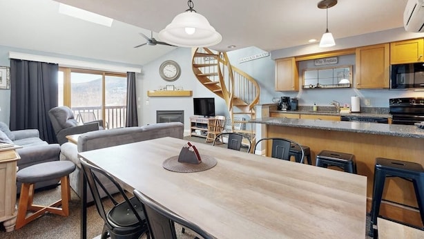 Eine moderne Küche mit Wendeltreppe, einem Essbereich mit Holztisch und einem Wohnzimmer mit Sofa und Fernseher.