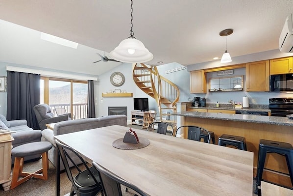A modern kitchen with a spiral staircase, a dining area with a wooden table, and a living room with a sofa and TV. - Mountain stunner with pools, hot tub, tennis, grilling area, & game tables (Bartlett)
