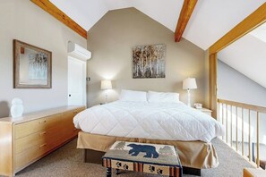 A bedroom with a large bed, wooden headboard, a bedside table with a lamp, a dresser, and a small bench with a bear design. - Mountain stunner with pools, hot tub, tennis, grilling area, & game tables (Bartlett)