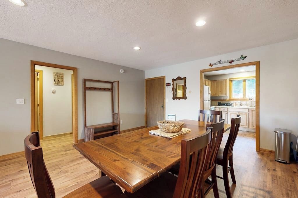A dining area with a wooden table and chairs, a kitchen visible through an open doorway, and a trash can near the kitchen.