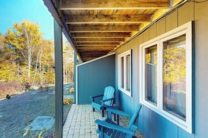 Eine überdachte Veranda mit zwei Adirondack-Stühlen, einem Steinweg und Blick auf Herbstbäume.