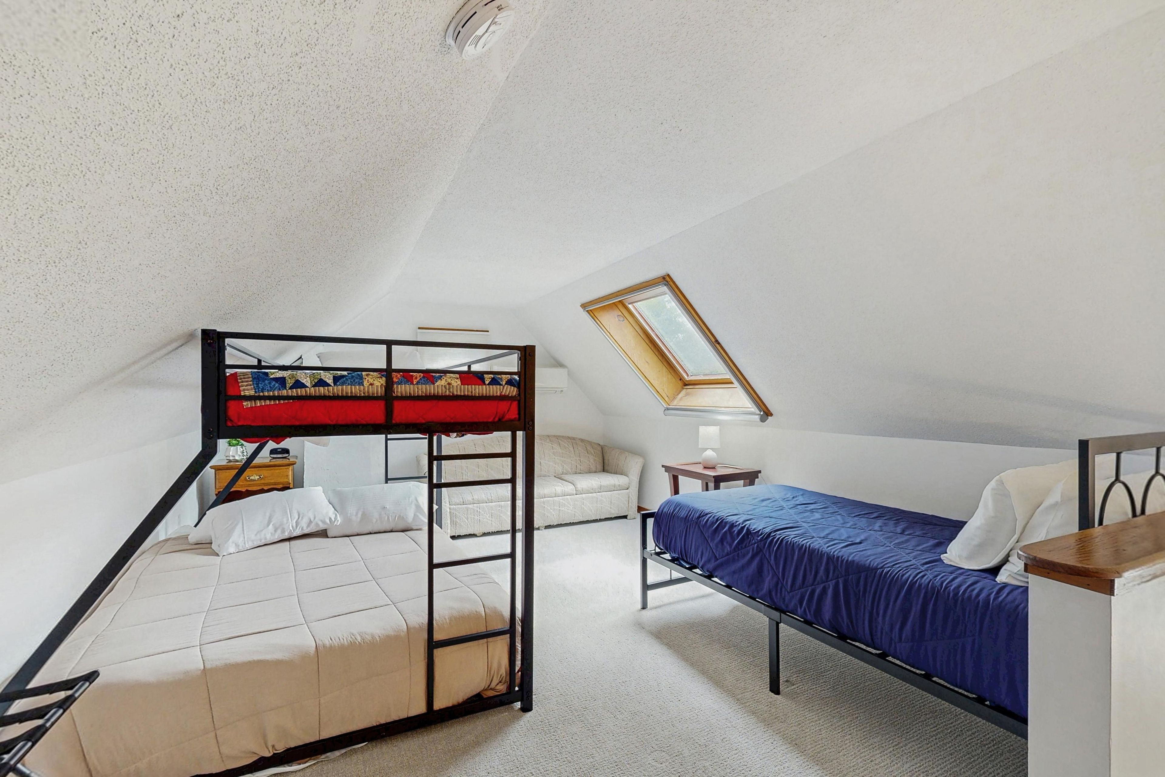 Ein Schlafsaalzimmer mit Etagenbetten, einem Einzelbett, einem kleinen Tisch, einem Stuhl und einem Dachfenster.
