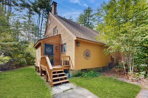 Une cabane en bois avec un toit à forte pente, une véranda à l’avant avec des marches et une cheminée.