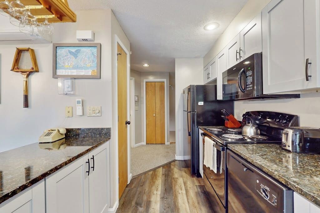 Una cocina moderna con armarios blancos, encimera de granito, refrigerador de acero inoxidable, microondas, estufa y lavavajillas.