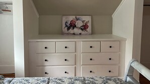 Ein Schlafzimmer mit einem Bett, einer weißen Kommode mit Schubladen und einem Blumenbild an der Wand.