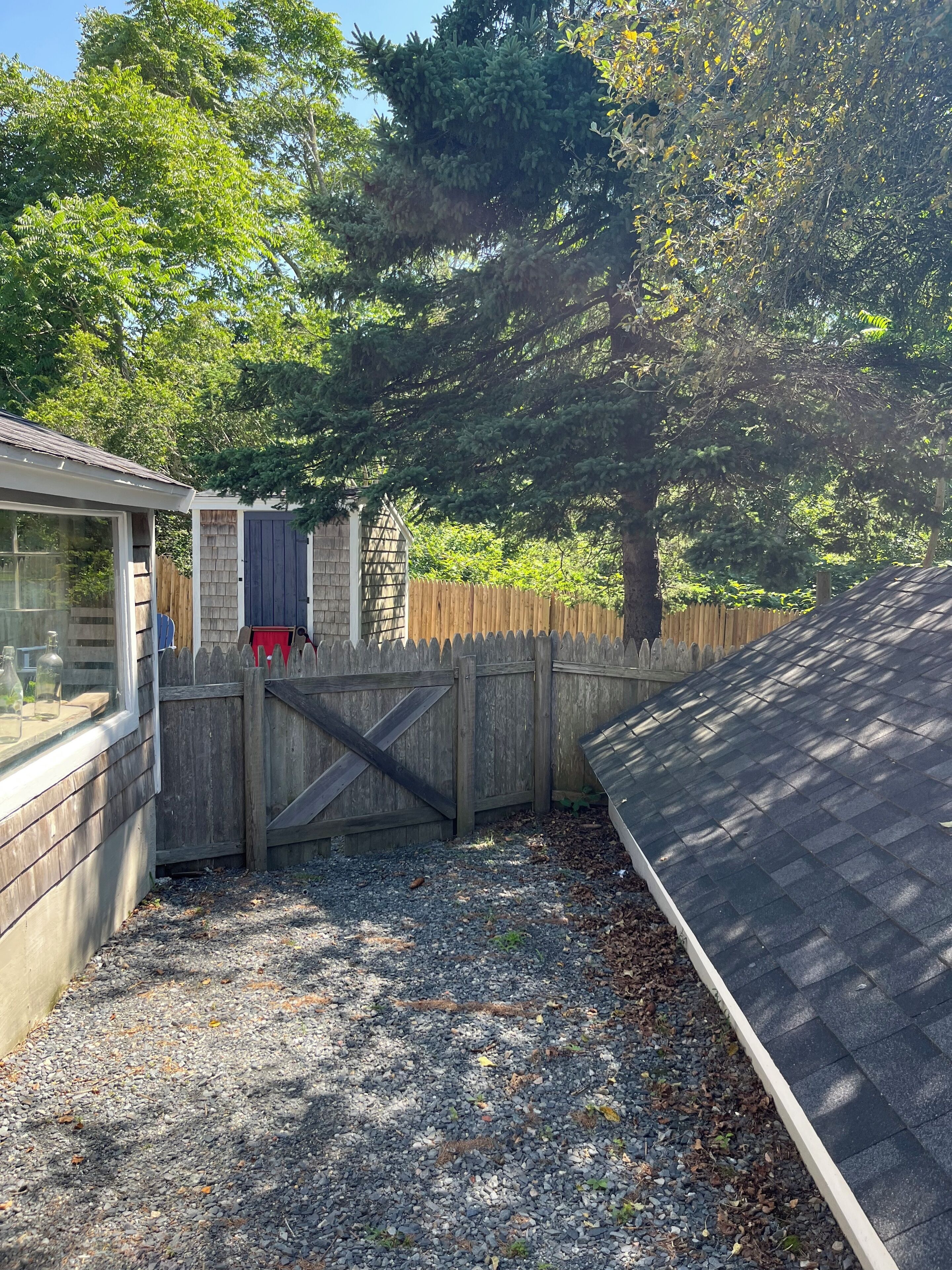 Ein Garten mit Holzzaun, Gartenhaus und Kiesfläche.