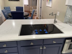 A kitchen with a black stovetop, a white marble countertop, and dark blue cabinets with gold handles. - Bring Fido! Spacious 2 family home 7-bedroom 5 bathroom in charming Chatham. (Chatham)