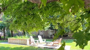 Ein Gartenbereich mit einem Holzbeet, einer Sitzgruppe mit Stühlen und einem Rasen.