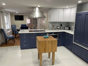 A modern kitchen with dark blue cabinets, a stainless steel range hood, and a central island with a wooden table. - Bring Fido! Spacious 2 family home 7-bedroom 5 bathroom in charming Chatham.🐶⛱️🛥️ (Chatham)