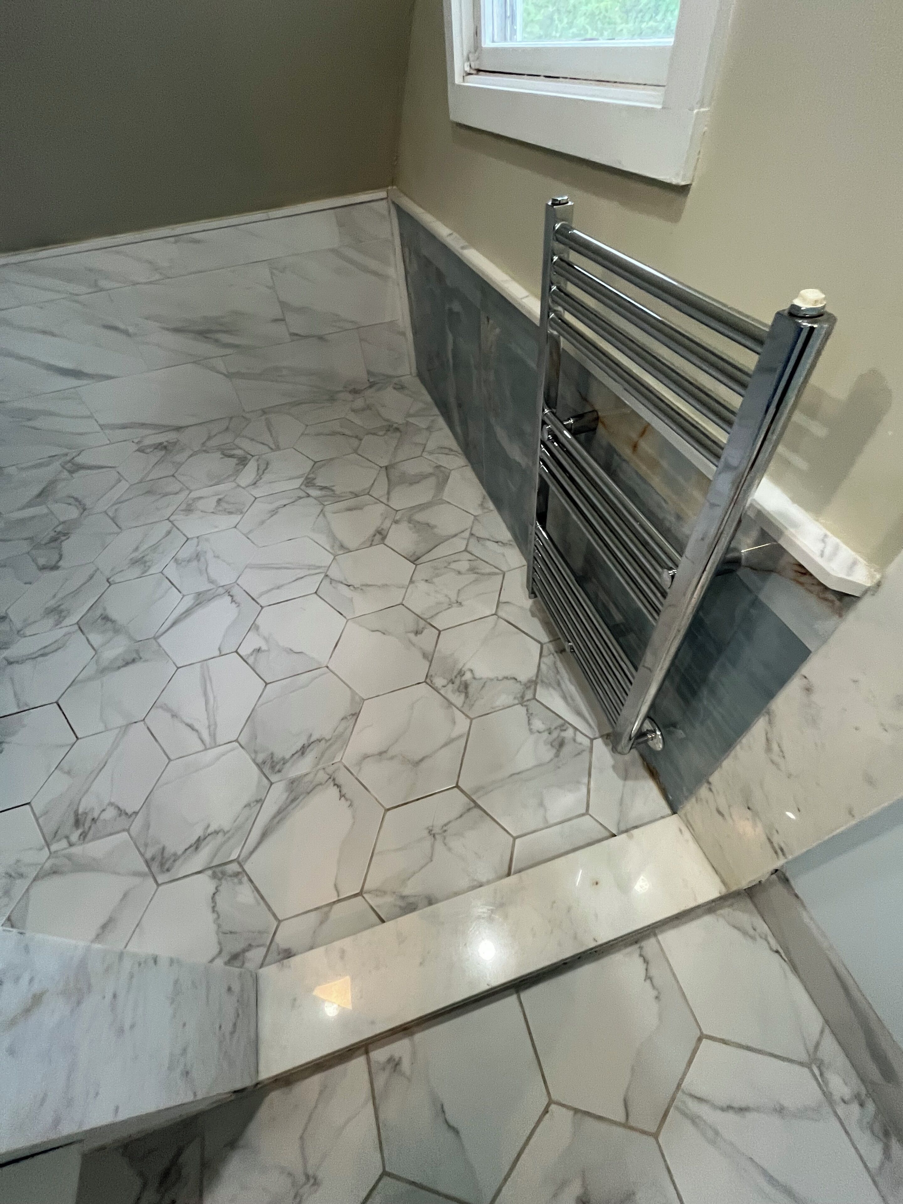 Un baño con baldosas de mármol hexagonales, un perchero y una ventana.