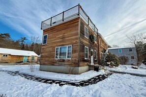 Une maison en bois à deux étages, dotée d’un balcon, d’un porche et d’une cour enneigée.