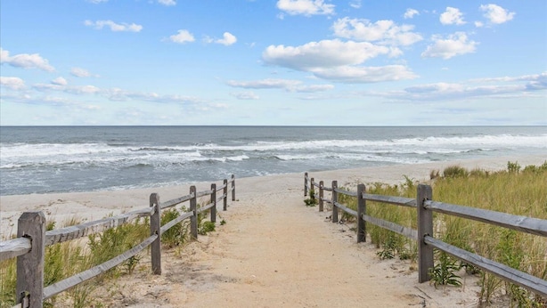 Een zandpad langs het strand dat naar de oceaan leidt, met een houten hek aan weerszijden.