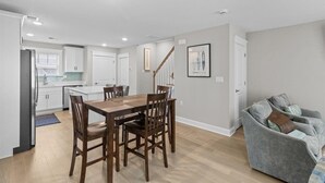 Een moderne keuken met witte kastjes, een eettafel met stoelen, een grijze bank en een trap.