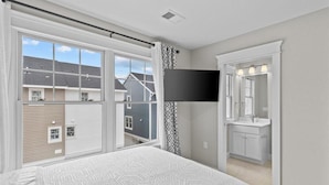 Een slaapkamer met een groot raam, een flatscreen televisie, een badkamer met wastafel en spiegel, en een bed met een decoratieve spreidek.